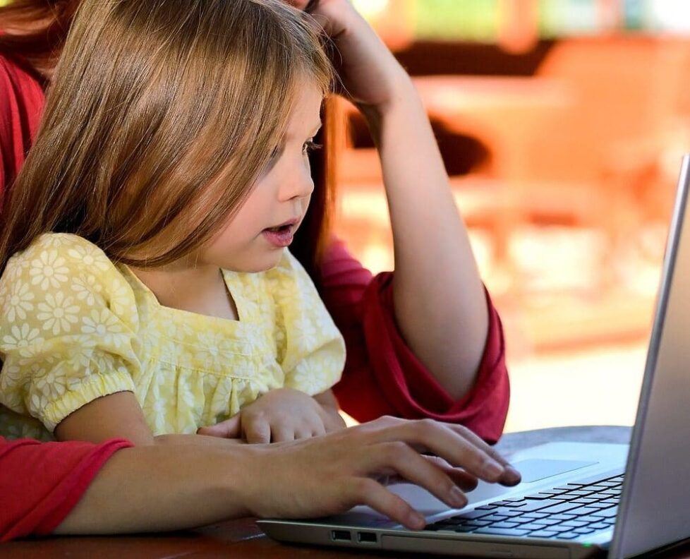 A child participating in online speech therapy with her mother.